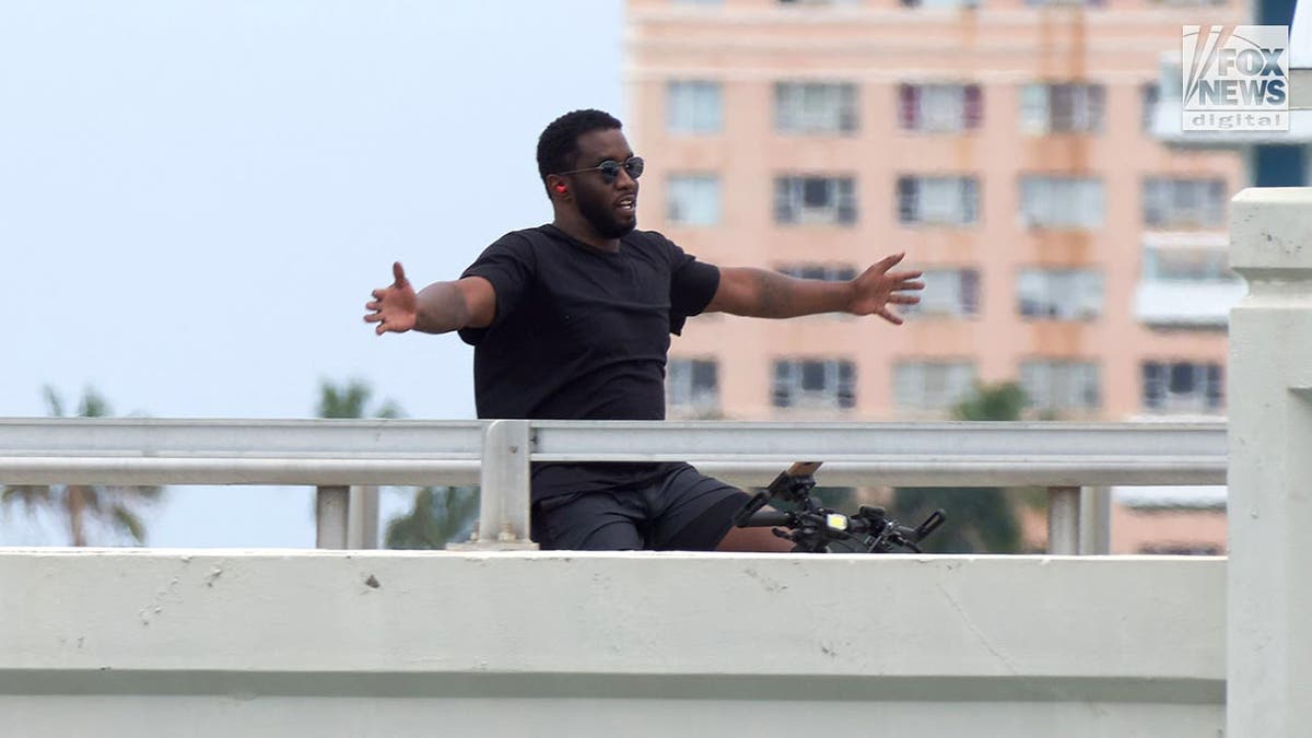 P Diddy rides has bicycle pinch arms outstretched wearing sunglasses.