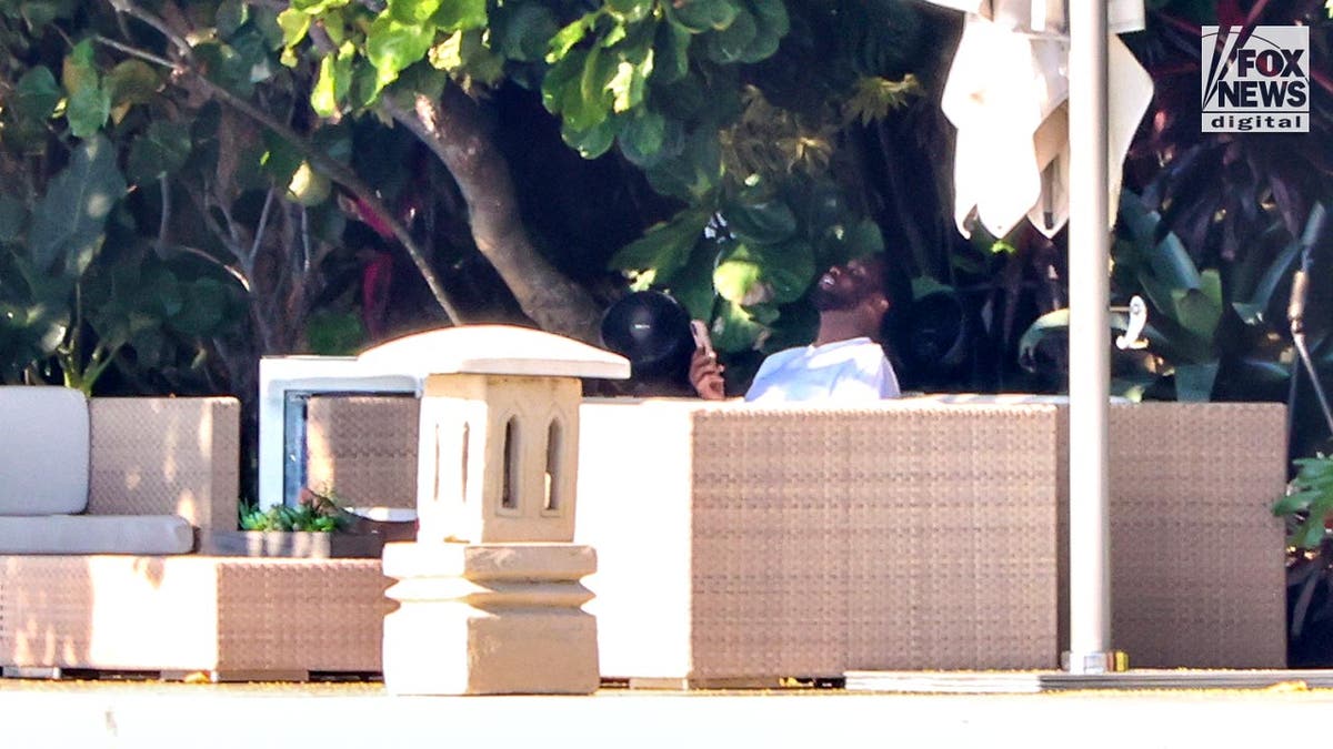 Sean "Diddy" Combs sits on his couch outside his Star Island laughing while on his phone