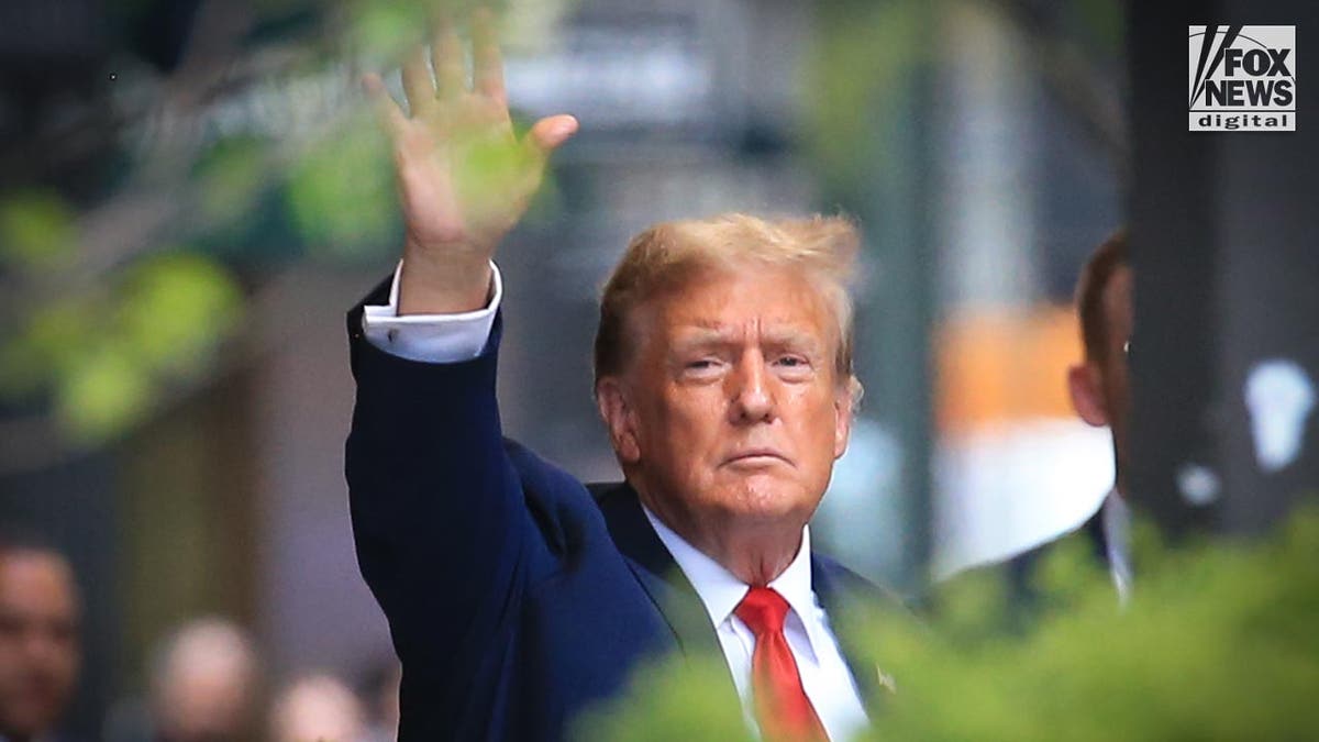 Trump waves, dressed in a blue suit and red tie.