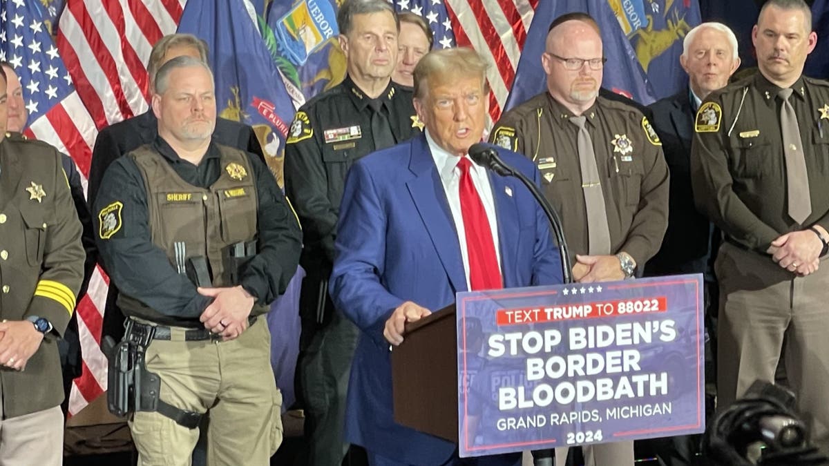 Trump speaking with law enforcement officers, flags behind him