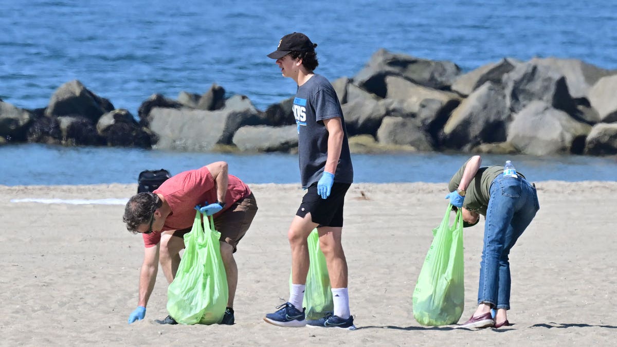 Three people are seen helping pick up trash at Venice Beach for Earth Day, 2023.