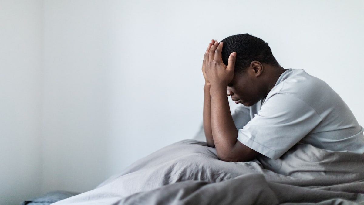 Man laying in bed with his hands on his head.