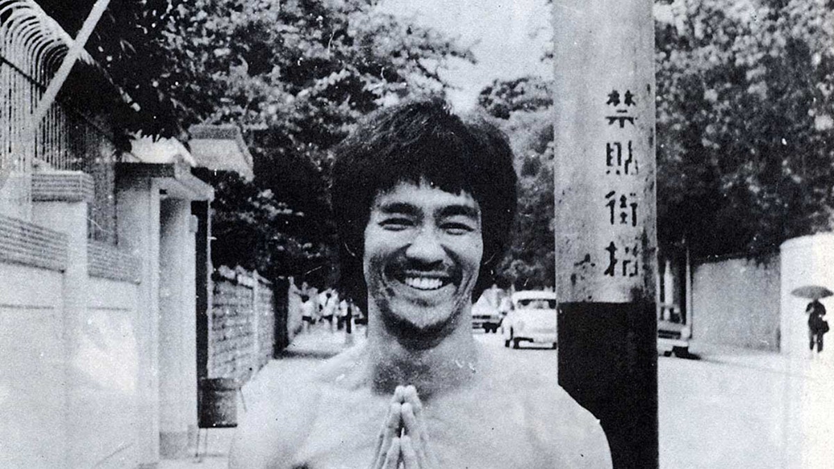 Bruce shirtless, smiling, hands together, pray motion, beard, standing in the street.