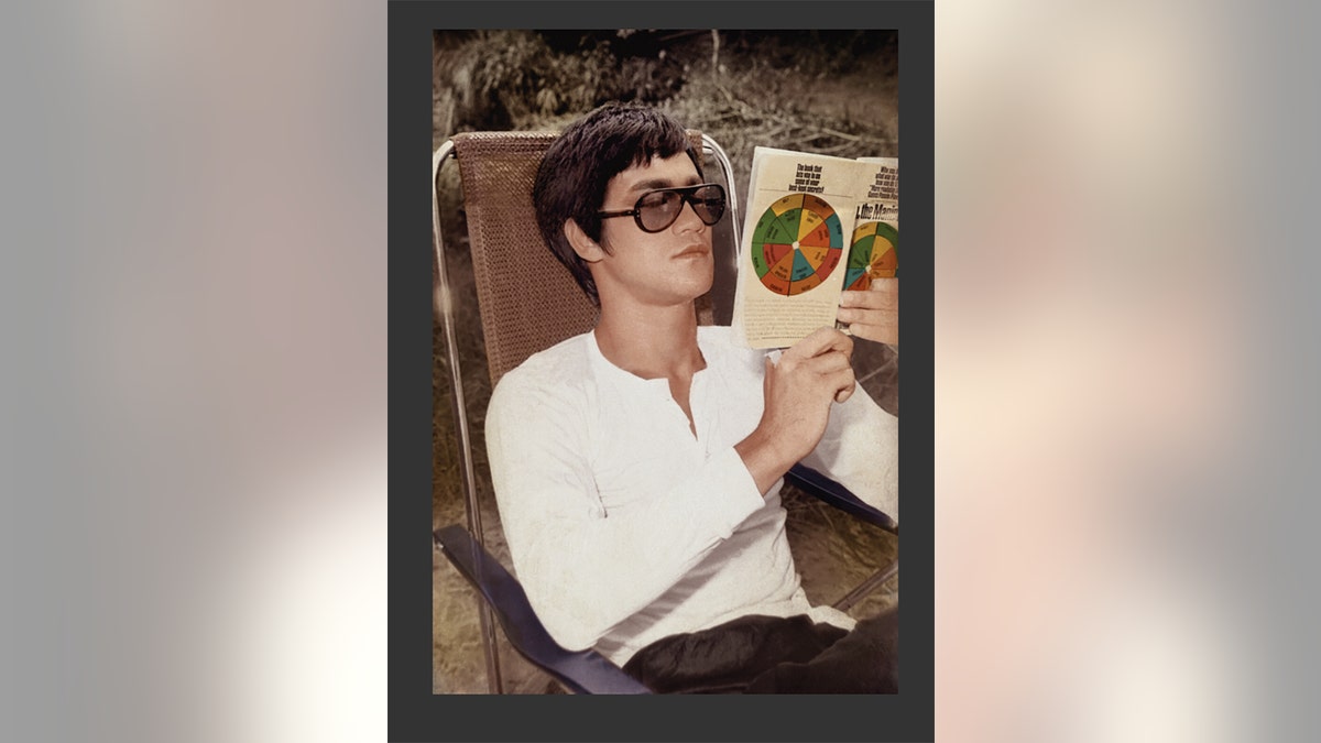 Bruce Lee reading a book from a chair