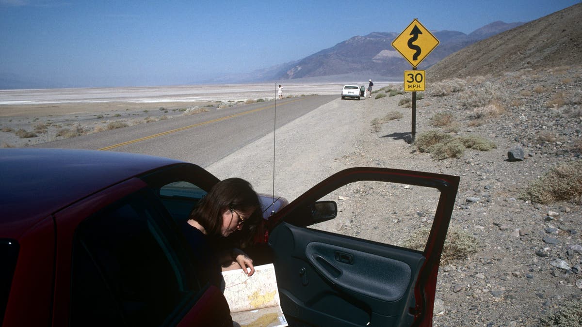 A woman is standing on the side of the road reading a map