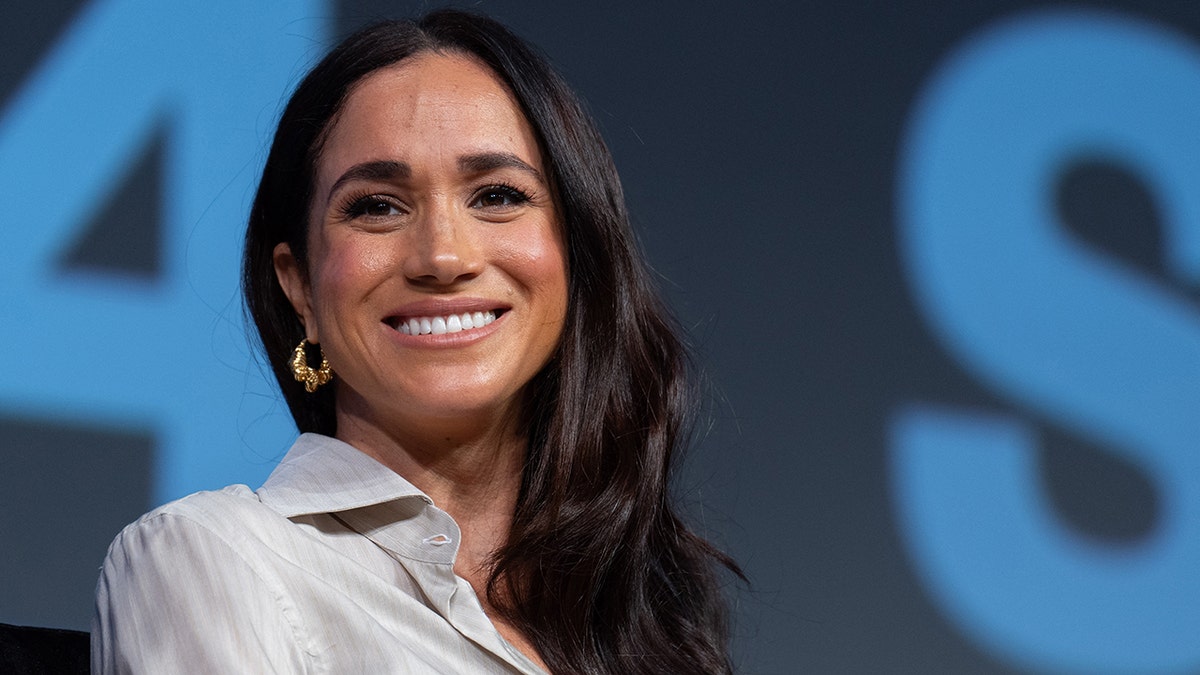 A close-up of Meghan Markle smiling and looking to her side