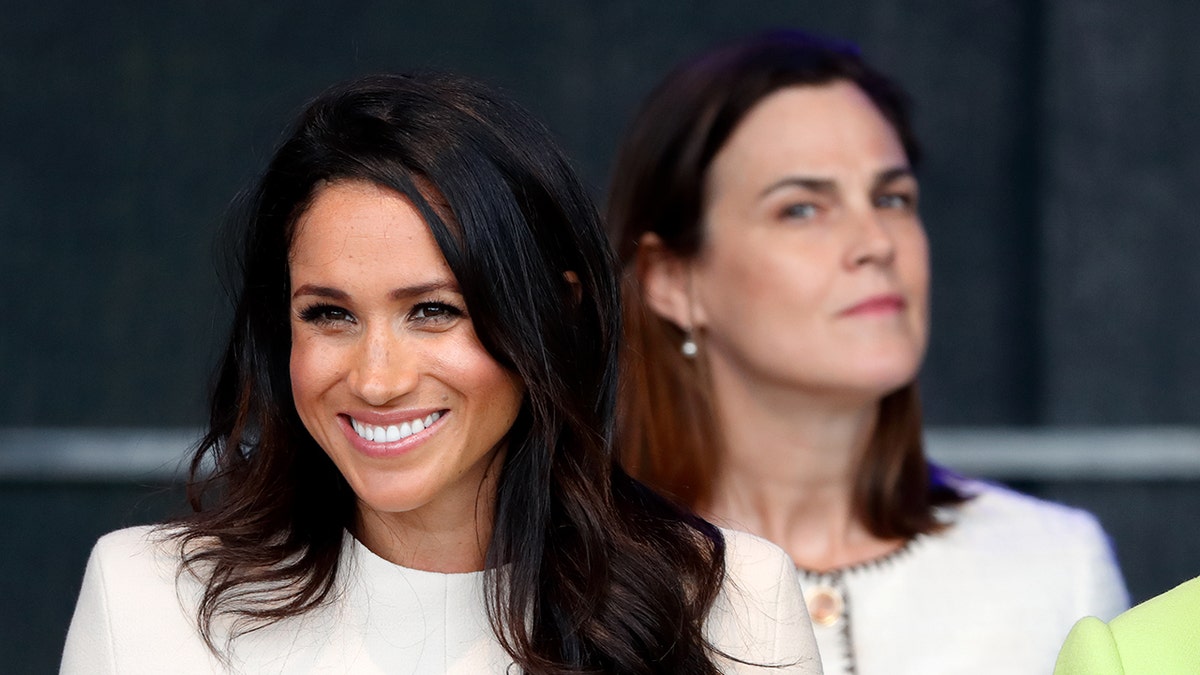 Samantha Cohen looking down a smiling Meghan Markle