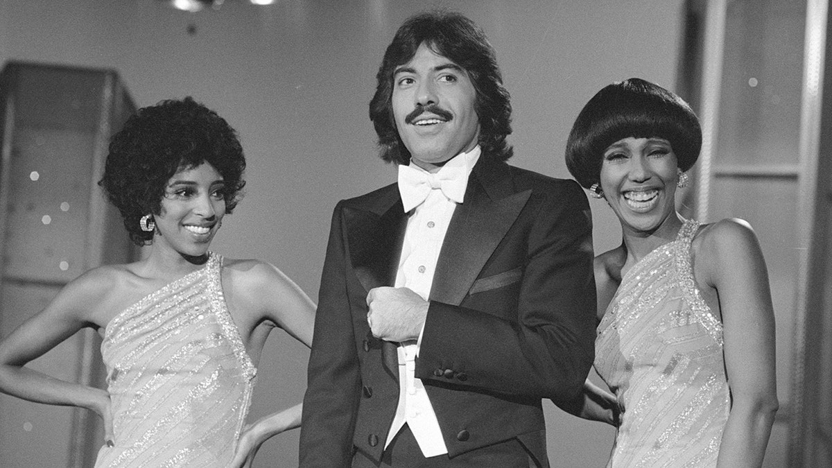 Tony Orlando in a suit and bow tie standing in between two smiling women