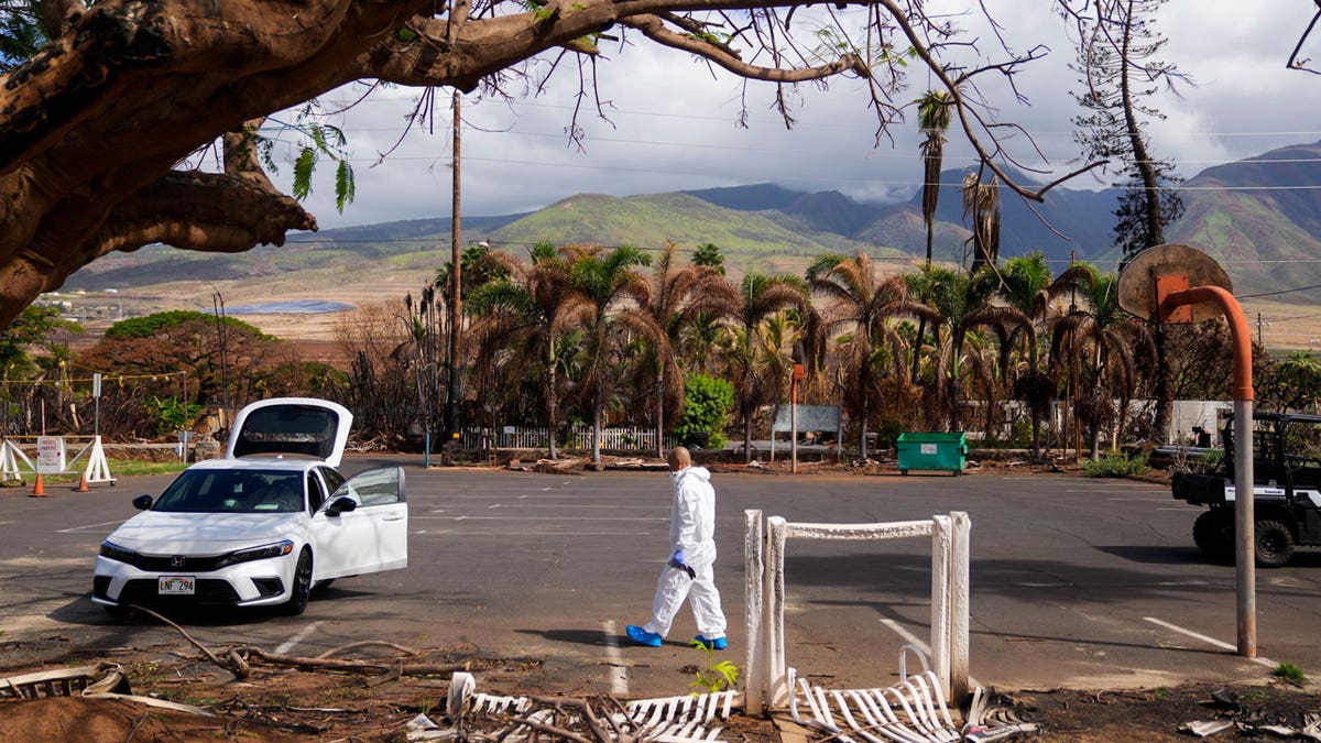 The Rev. Ai Hironaka, resident minister of the Lahaina Hongwanji Mission, walks in the parking lot wearing a protective white suit as he visits his temple and residence destroyed by wildfire