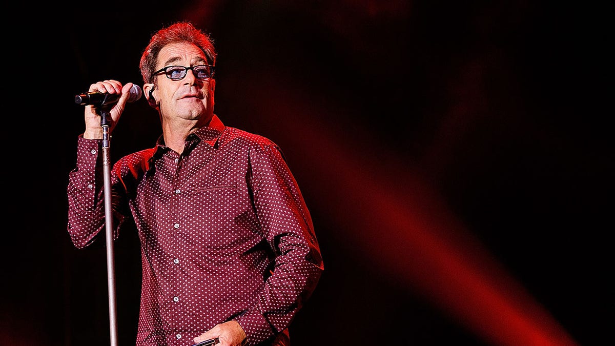 Huey Lewis standing at microphone on stage