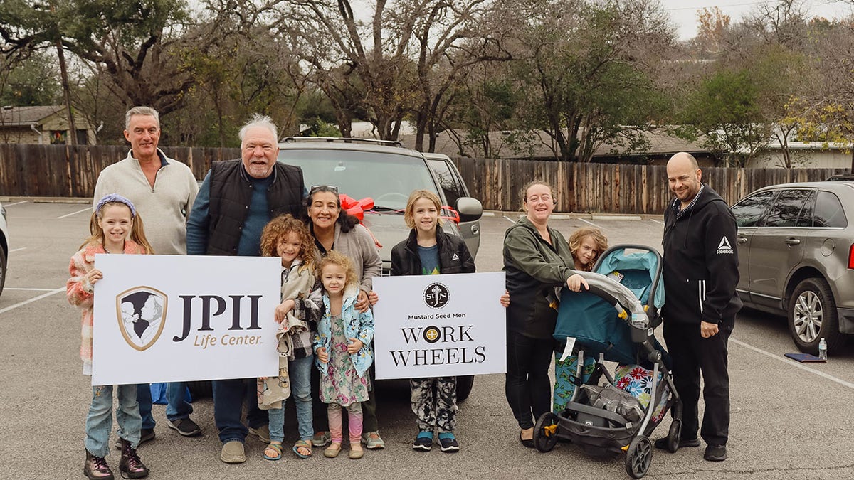 people successful beforehand of car holding signs for "Work Wheels" and "JPII Center"
