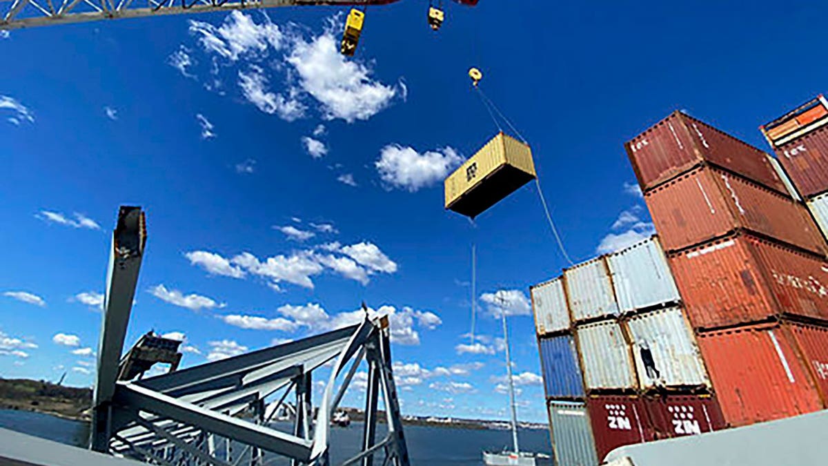 Response crews begin removing shipping containers from the deck of the cargo ship Dali using a floating crane barge at the site of the Francis Scott Key Bridge