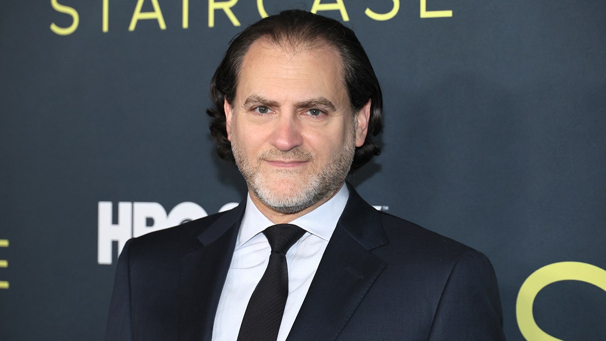 Michael Stuhlbarg in a black suit and tie soft smiles on the carpet