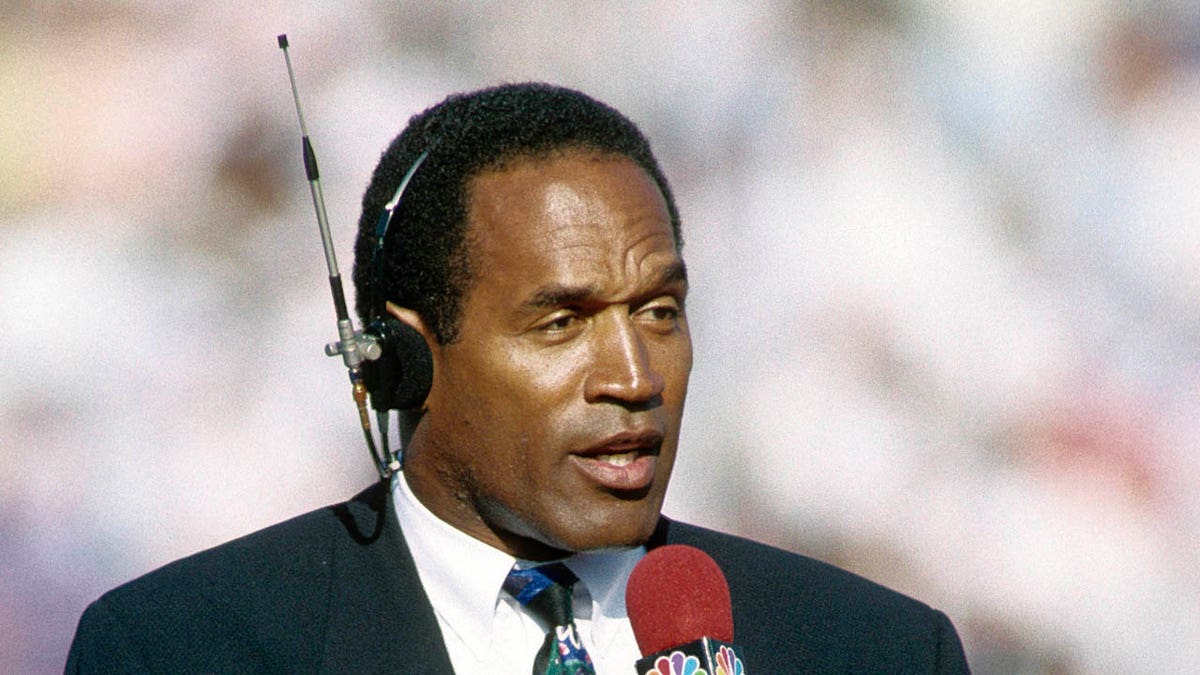 O.J. Simpson standing in a broadcast booth at the Rose Bowl stadium.