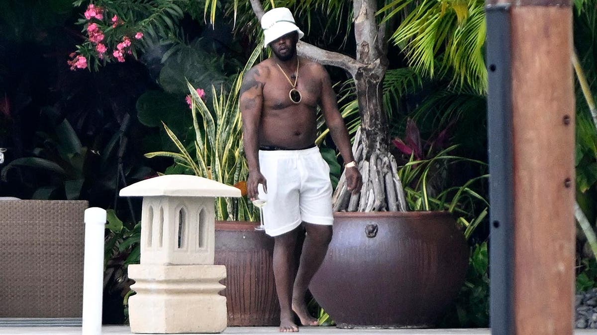 P Diddy is on his waterfront spot at his home in Miami without a shirt on and carrying a wine glass