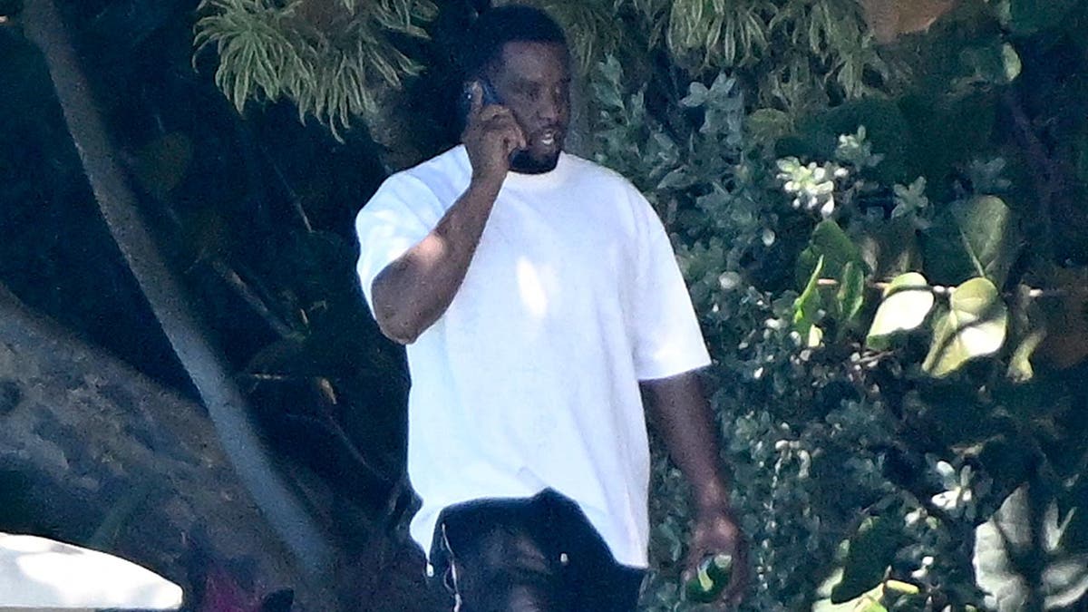 Sean Combs walks in a white t-shirt outside his Miami home on the phone
