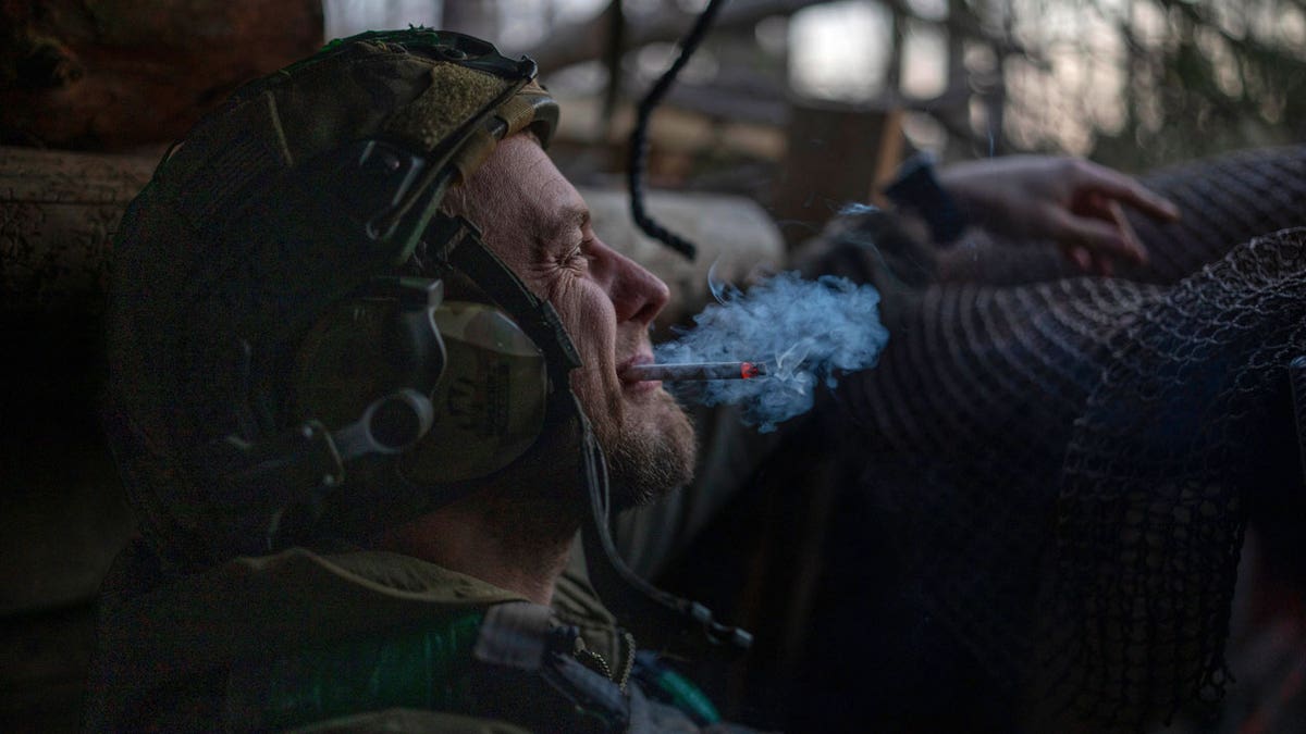 A Ukrainian serviceman from nan Azov brigade, known by nan telephone motion Chaos, smokes a cigaret successful a dugout while he waits for a bid to fire