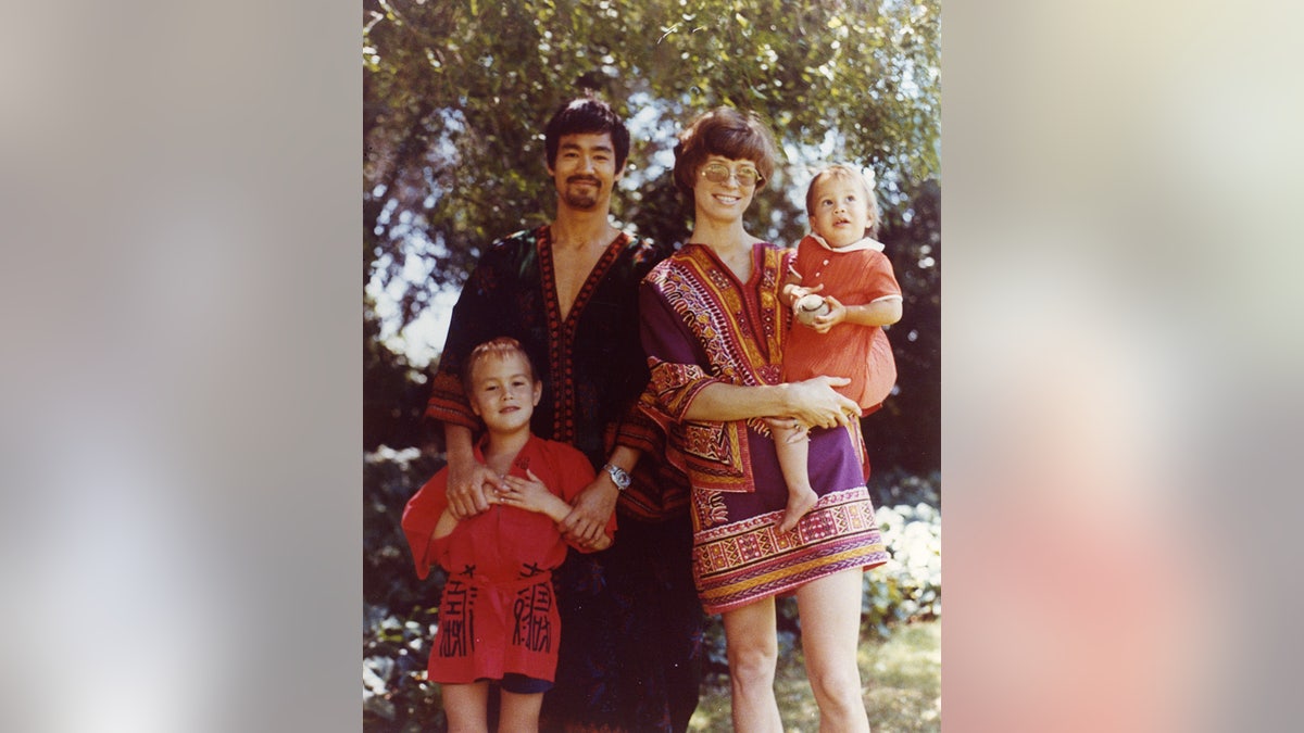 Family portrait, Bruce, Brandon, Linda, Shannon. Bruce is wearing a acheronian kaftan, beard, smiling, manus connected Brandon, while Linda holds Shannon. Tree and writer successful background.