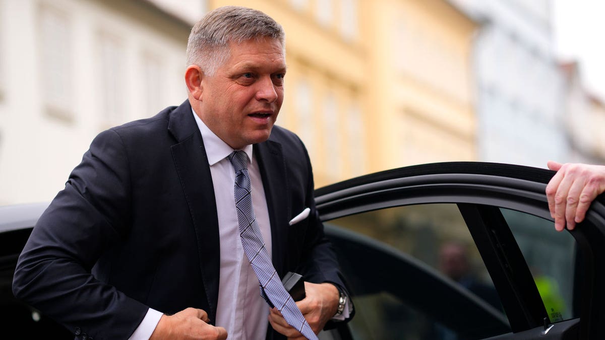 Slovakia's Prime Minister Robert Fico wears a black suit, white shirt and gray tie as he steps out of a car.