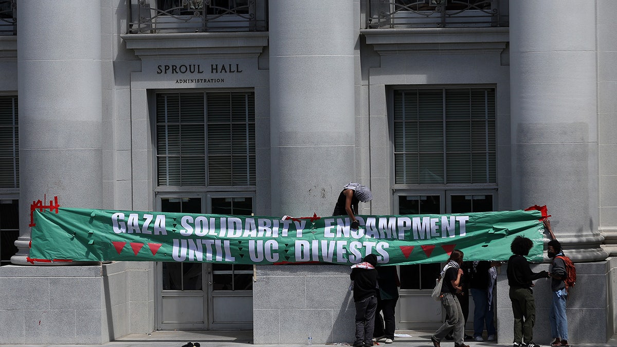 Pro-Palestinian protesters hang a banner as they set up a tent encampment in front of Sproul Hall on the UC Berkeley campus