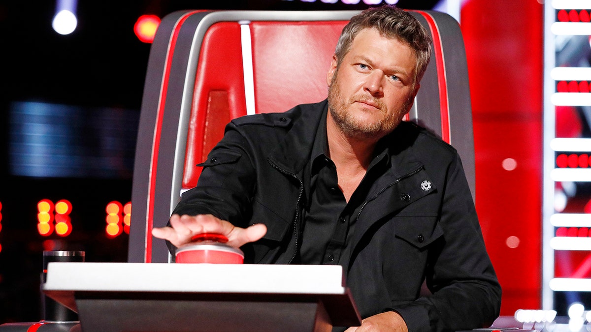 Blake Shelton in a black jacket presses his button to turn his chair on 'The Voice'