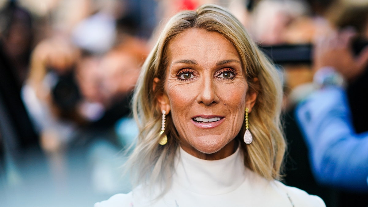 Celine Dion in a white turtleneck smiles on the carpet in France