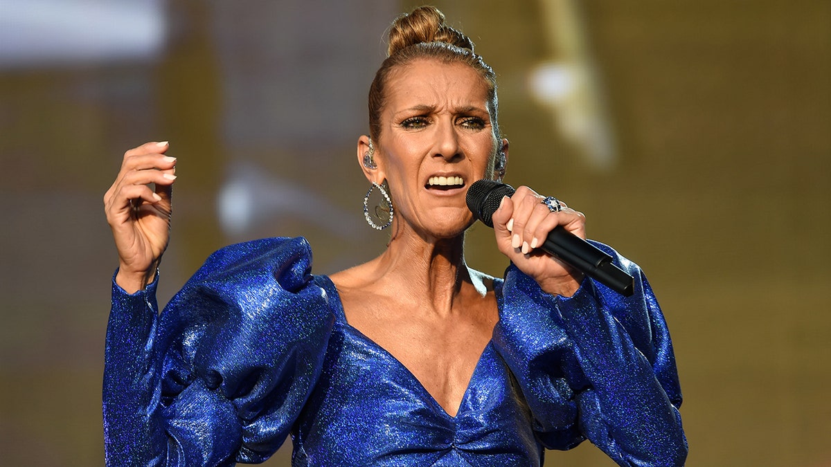 Céline Dion in a blue, shiny puffy blue dress sings passionately on stage