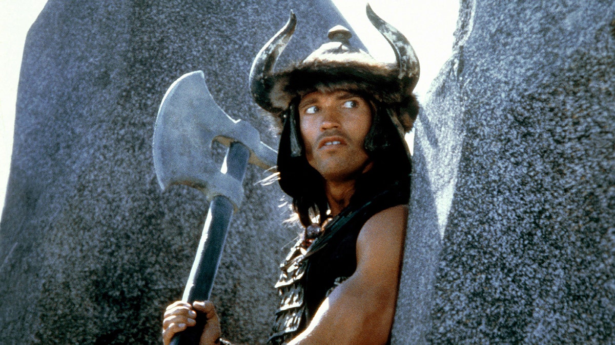 Arnold Schwarzenegger segurando um machado como Conan em 'Conan, o Bárbaro'