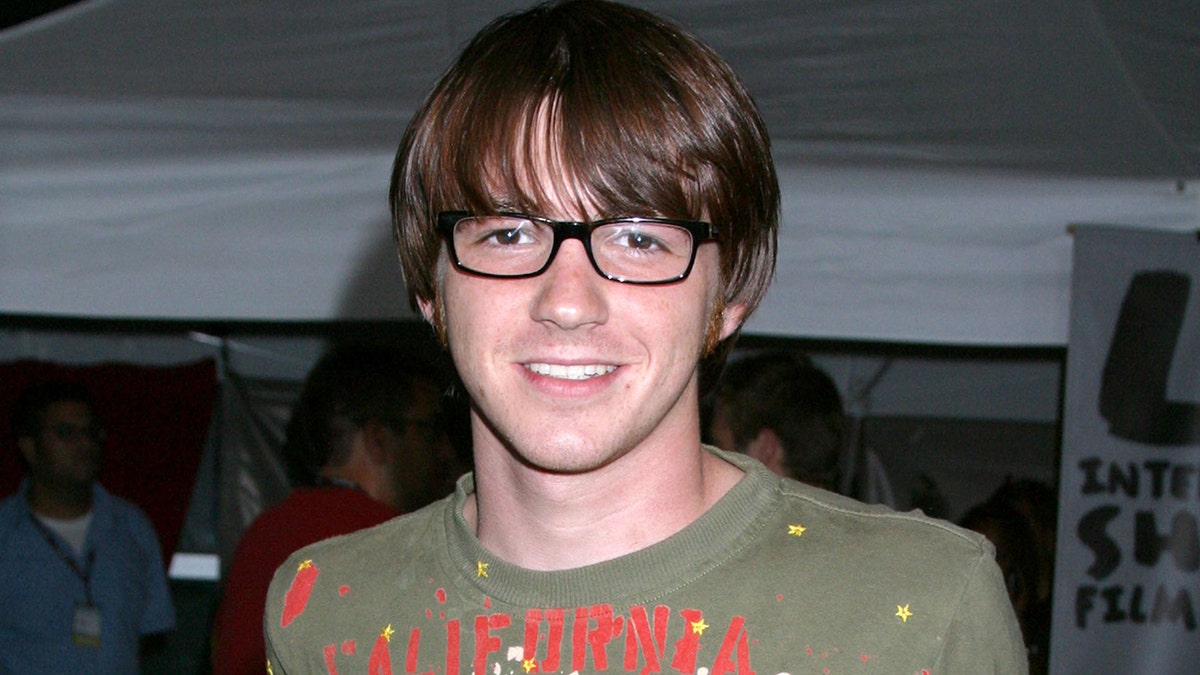 Drake Bell wearing a greenish garment and glasses successful 2004