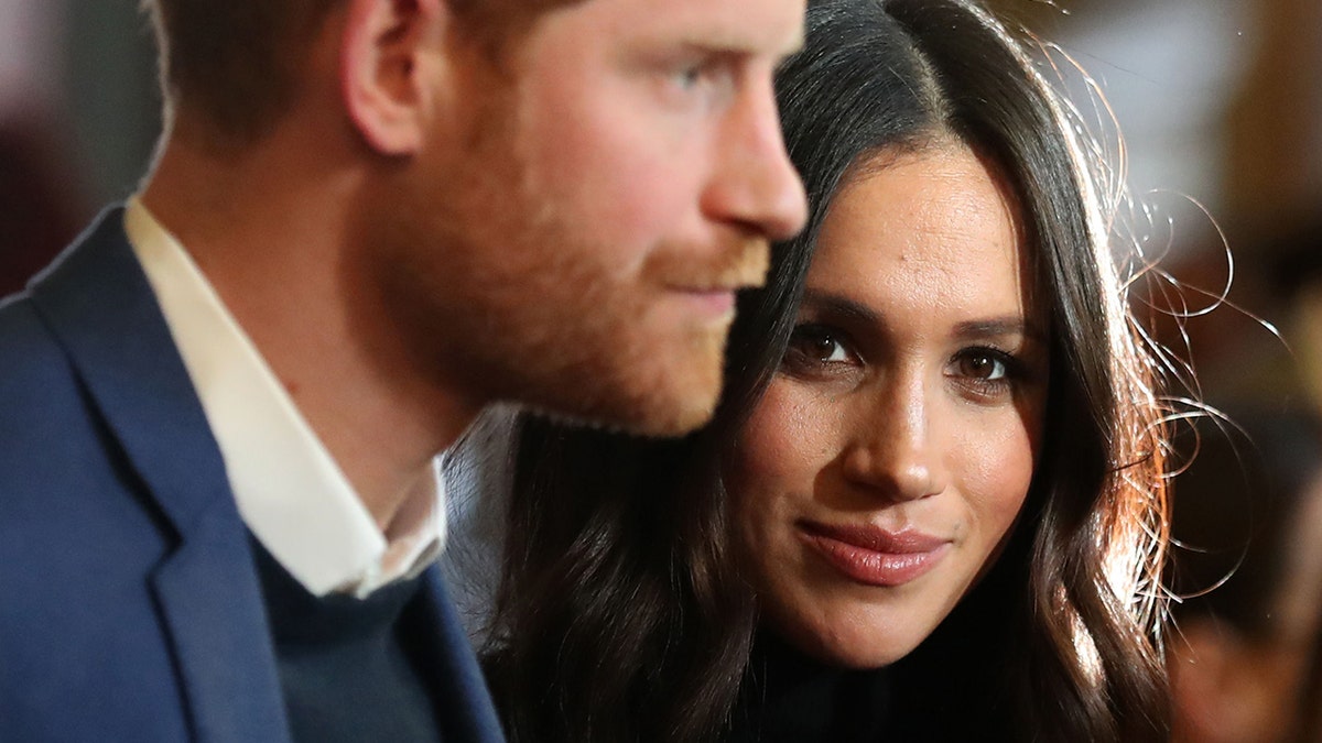Meghan Markle staring intently at the camera while Prince Harry looks ahead