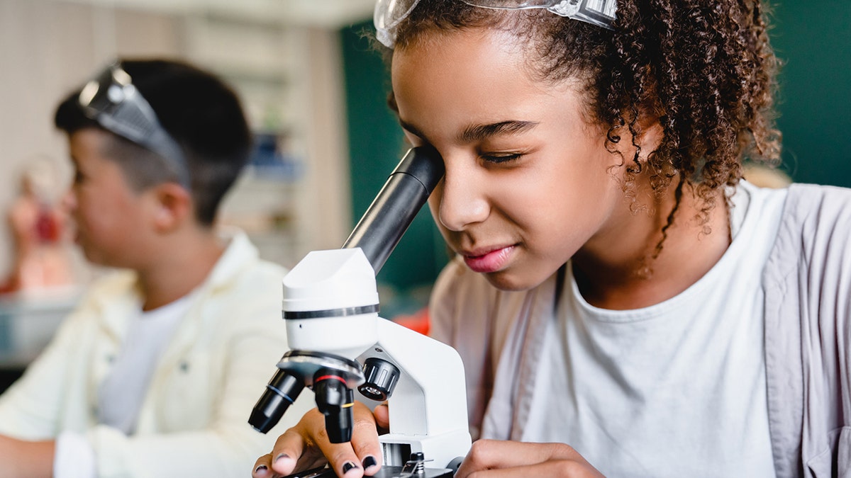 female student looks into microscope