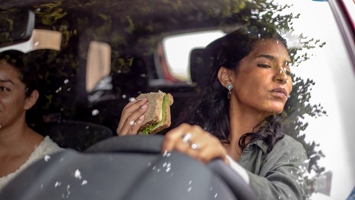 mulher dirige enquanto come um sanduíche