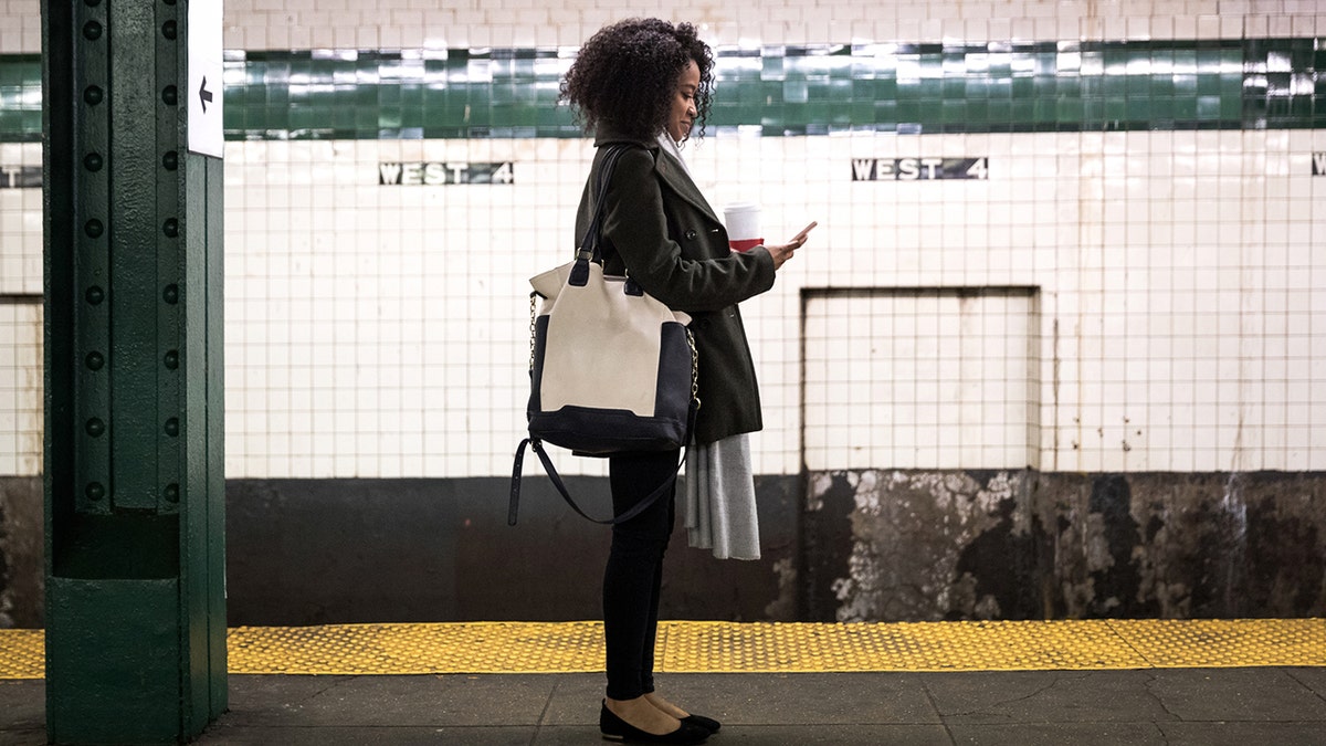 woman texts while waiting for a subway train