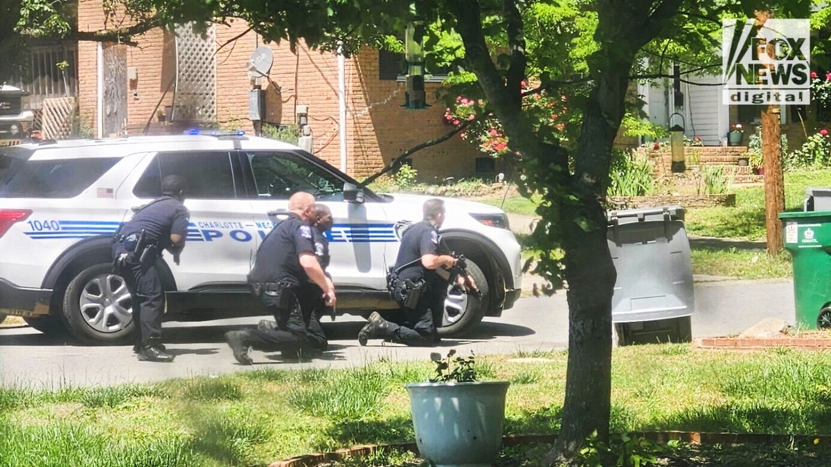 Charlotte officerS crouch behind a police vehicle on Galway Drive