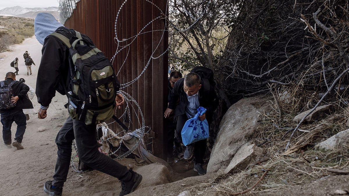 Migrants cross through a gap in the US-Mexico border fence in Jacumba Hot Springs