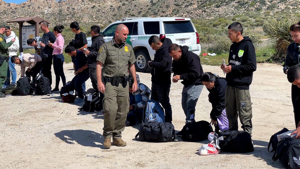 Border Patrol agent walks by line of migrants near Jacumba Hot Springs