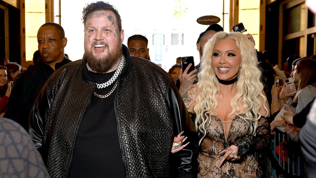 Jelly Roll em uma jaqueta de couro preta entra no iHeartRadio Music Awards com sua esposa Bunnie Xo em uma roupa preta de renda