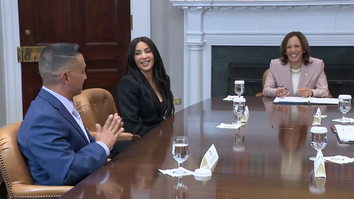 Kim Kardashian laughs as a pardon recipient tells his story and Kamala Harris sits at the table