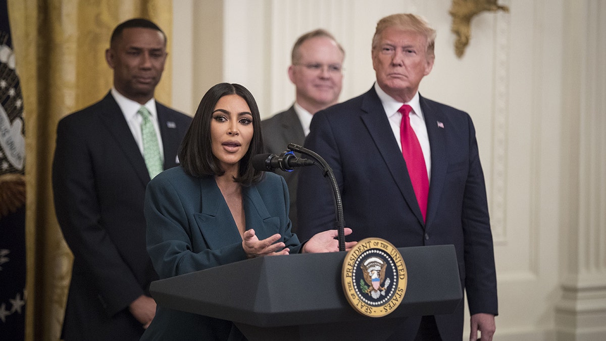 Kim Kardashian successful a acheronian teal suit stands down nan podium astatine nan White House pinch erstwhile President Trump successful a acheronian suit and reddish necktie opinionated to her left