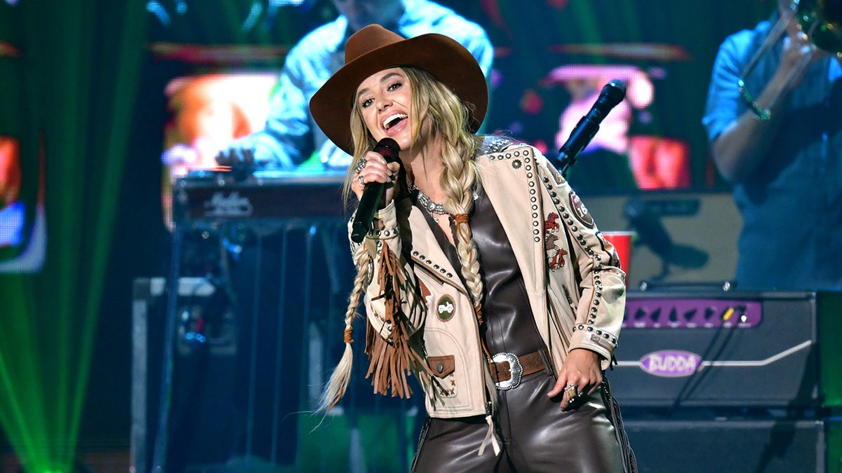 Singer Lainey Wilson rocks brown leather slacks and coat on stage at CMT Music Awards.