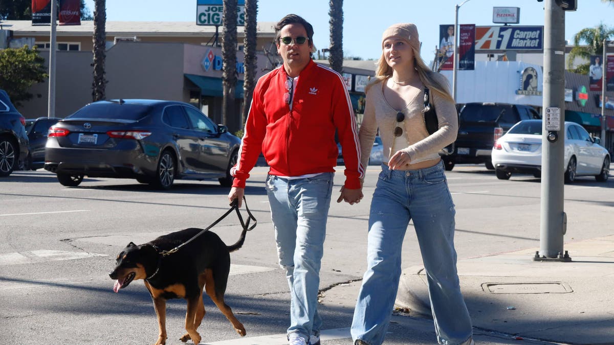 Ross McCall, wearing red jacket and blue jeans, walks hand-in-hand with Maggie Sajak, who's wearing a beaning, light jacket and blue jeans.