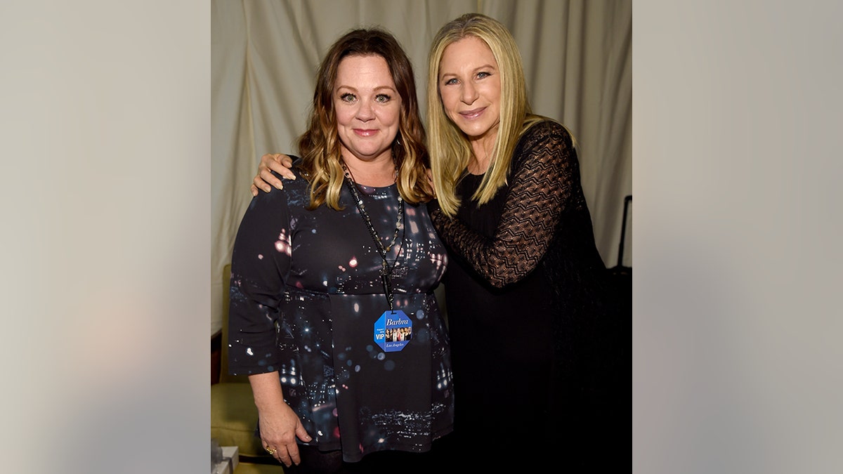 Melissa McCarthy successful a achromatic patterned dress has her shoulders hugged by Barbra Streisand successful black