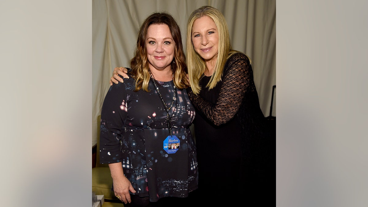 Melissa McCarthy con un vestido negro estampado se deja abrazar los hombros por Barbra Streisand de negro