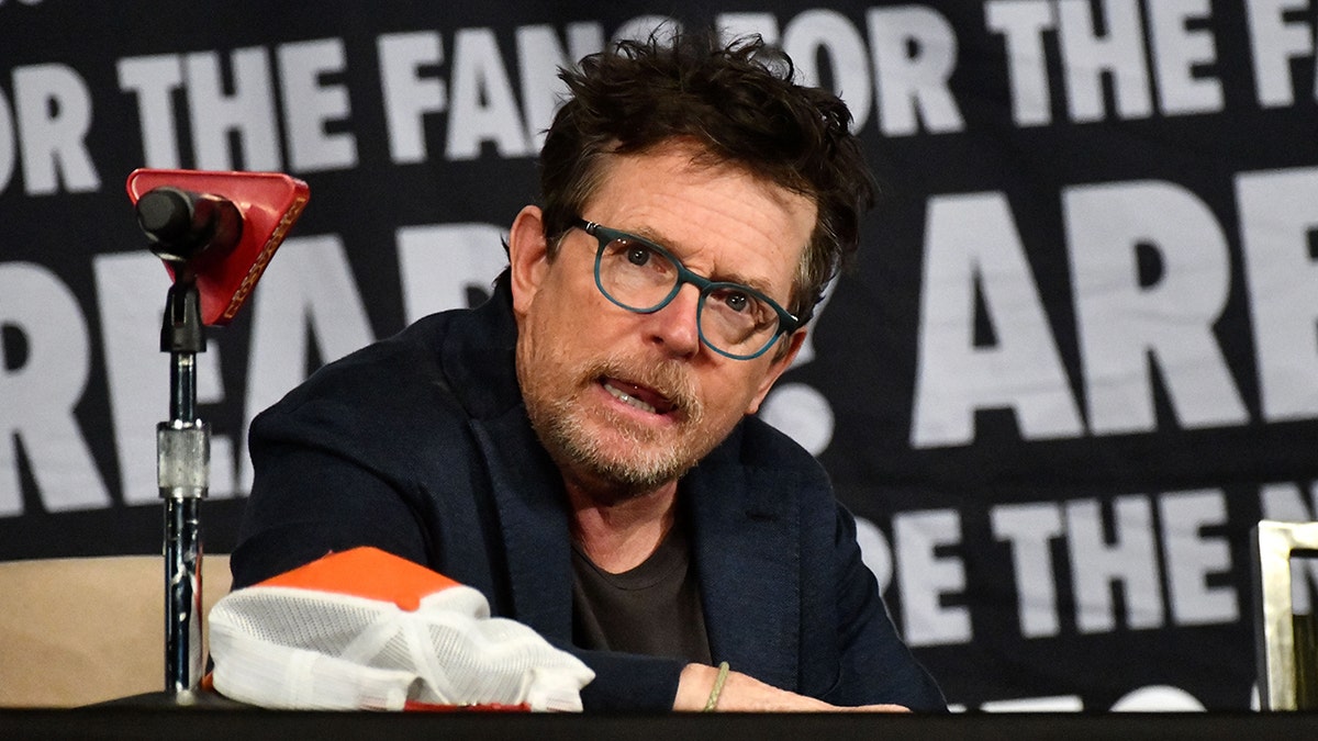 Michael J. Fox in a blue suit sits on a panel