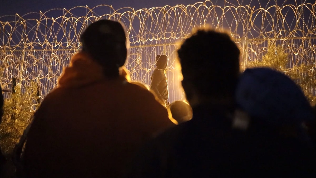 Migrants surging border wire fence at night