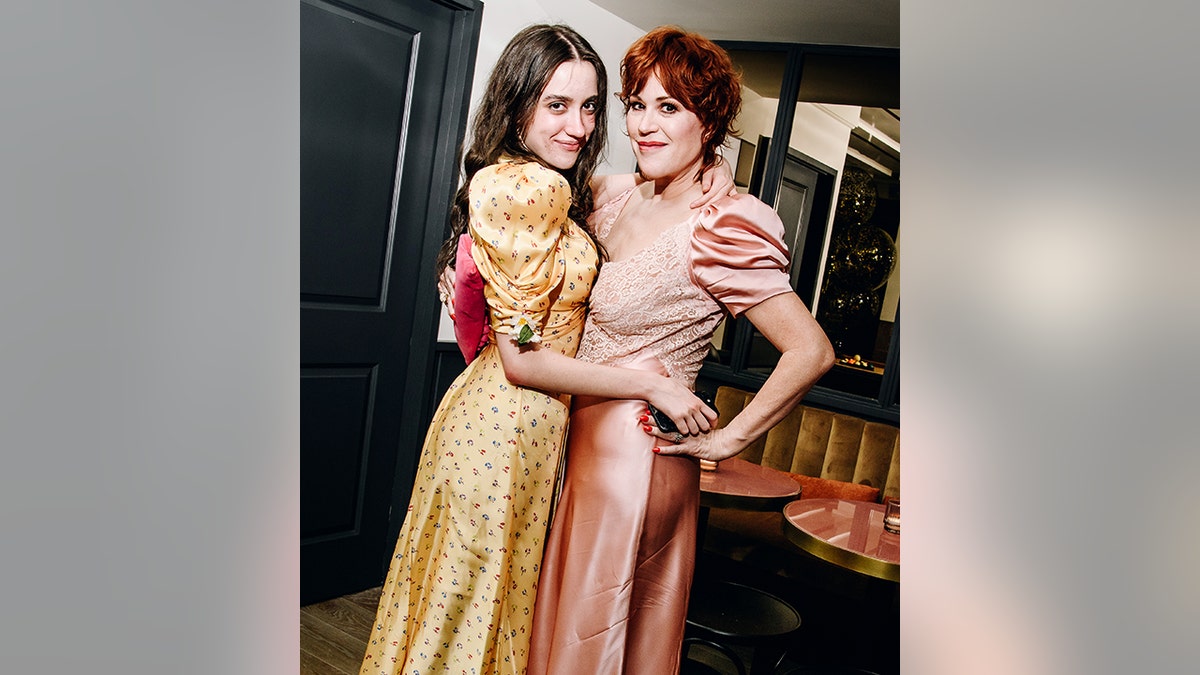 Molly Ringwald in a light pink dress with puffy sleeves wraps her arm around daughter Mathilda in a yellow dress with puffy sleeves