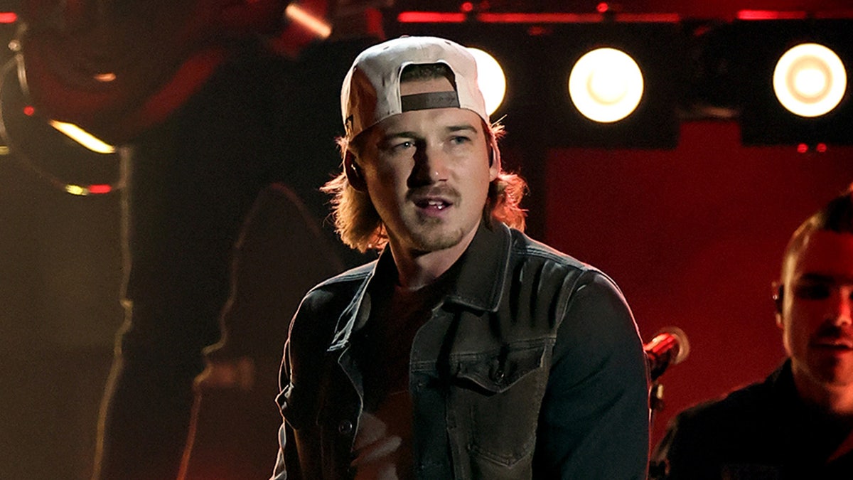 Morgan Wallen looks pensive as he looks out from onstage wearing a backwards hat