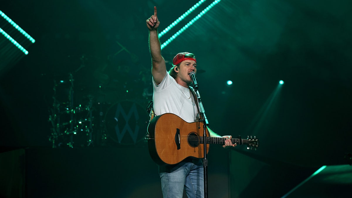 Bintang musik country Morgan Wallen memegang gitar saat konser.