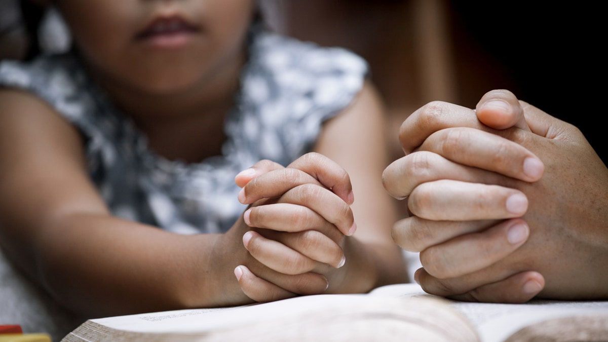 Mother and little girl's hands folded in prayer.
