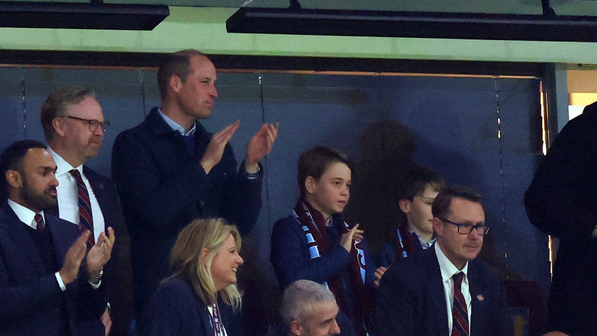 Prince of Wales wears buttoned up blue coat at soccer game with his son, Prince George.